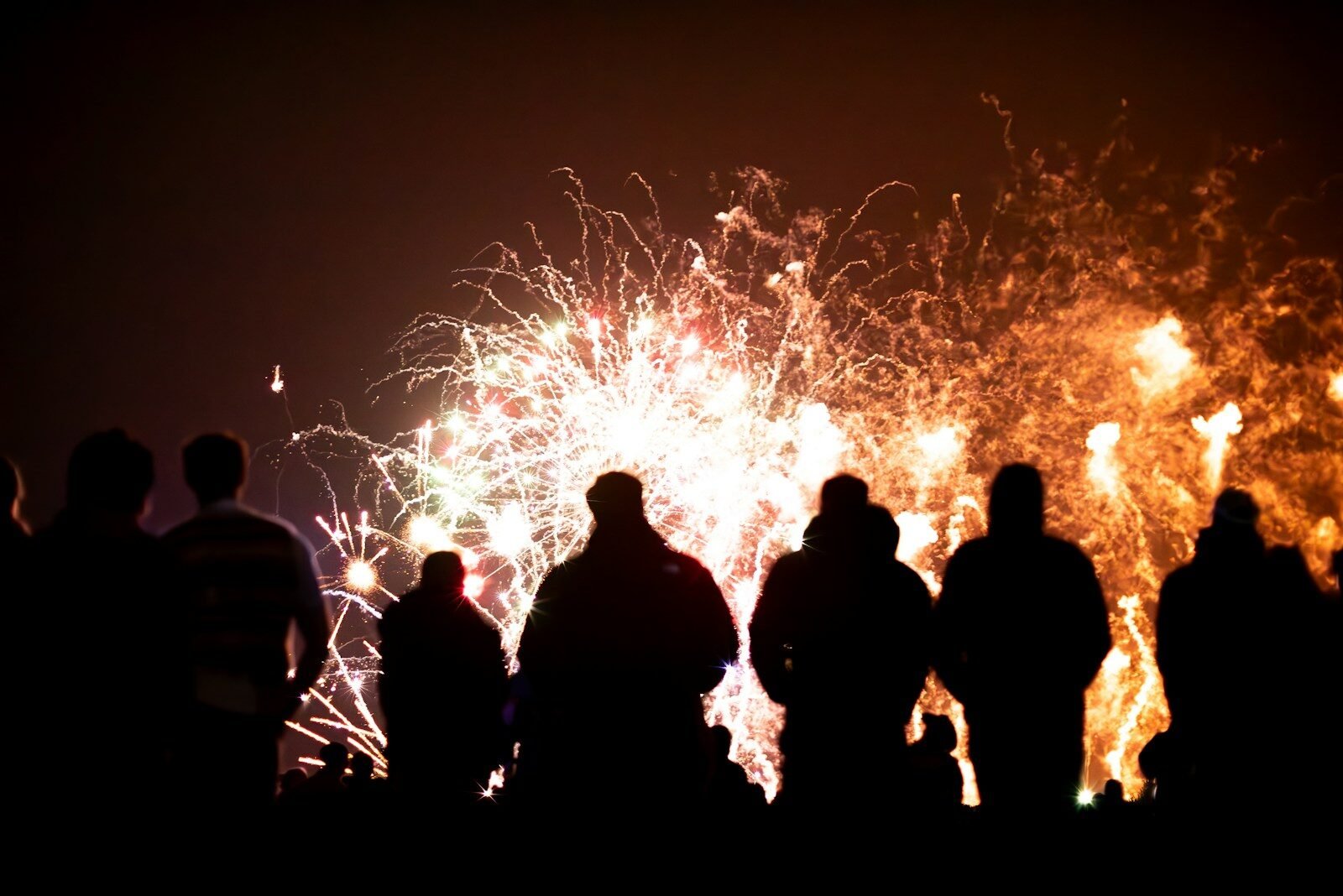 Silhouettes of people watching fireworks display at night
